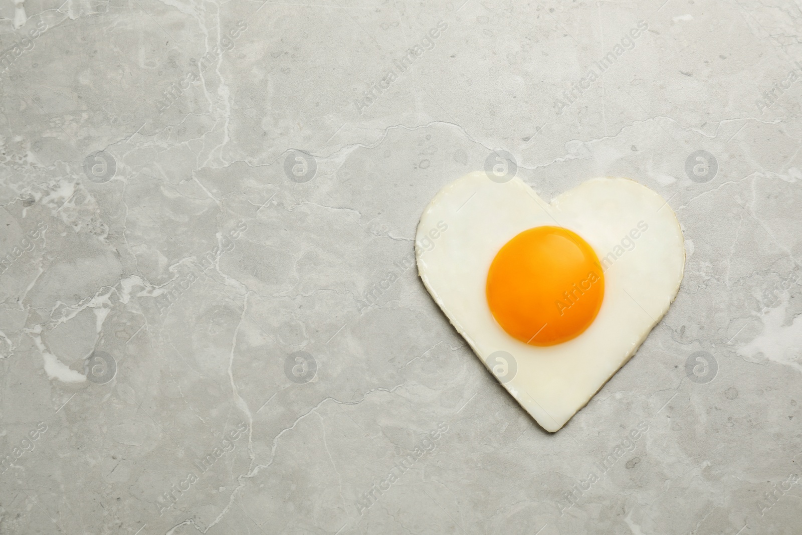 Photo of Tasty fried egg in shape of heart on marble table, top view. Space for text