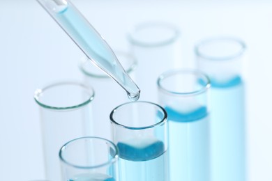 Dripping liquid from pipette into test tube on light background, closeup