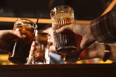 Group of friends clinking glasses with cola at table indoors, closeup