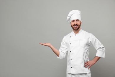 Photo of Mature chef showing something on grey background, space for text
