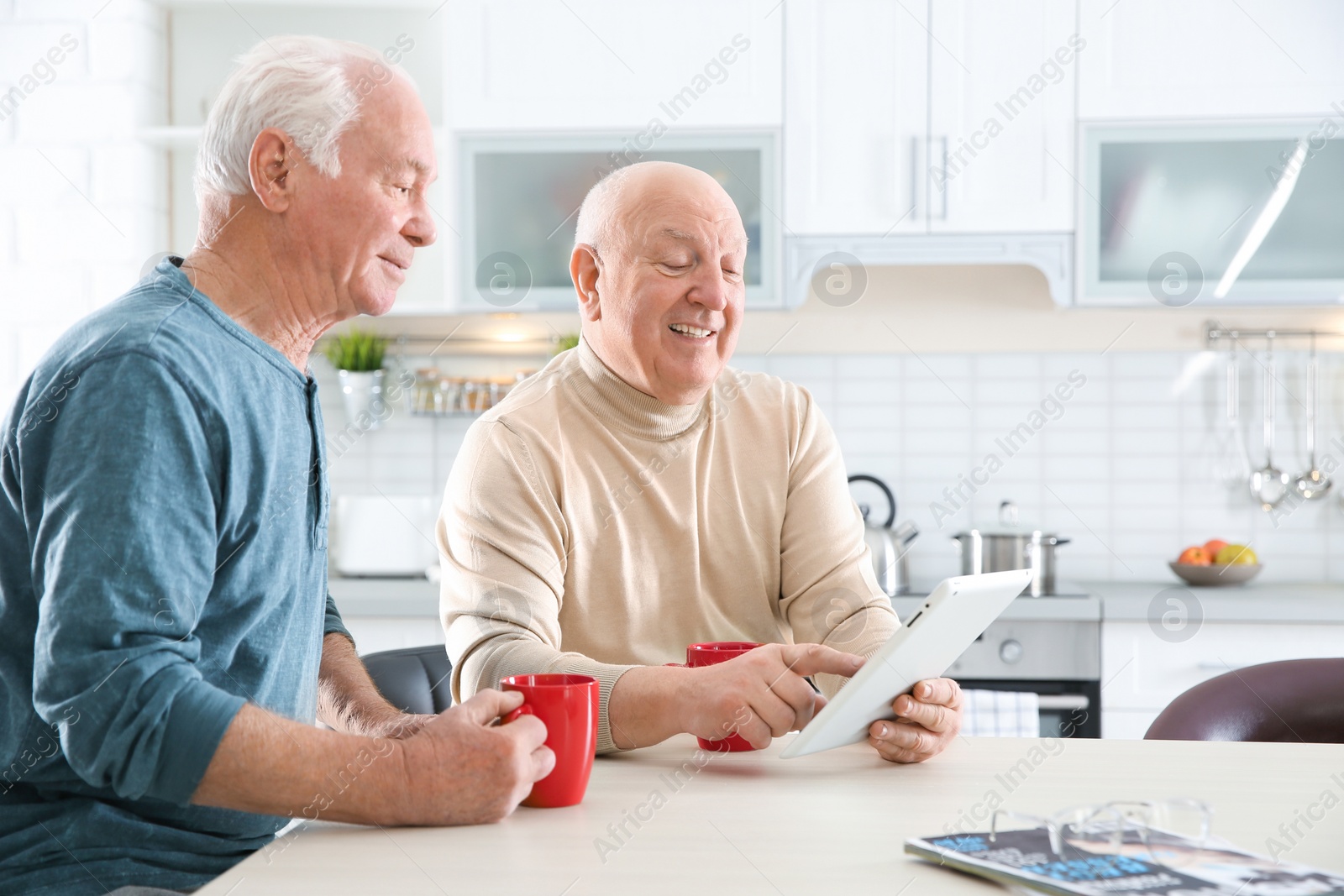 Photo of Elderly men using tablet PC at table in kitchen