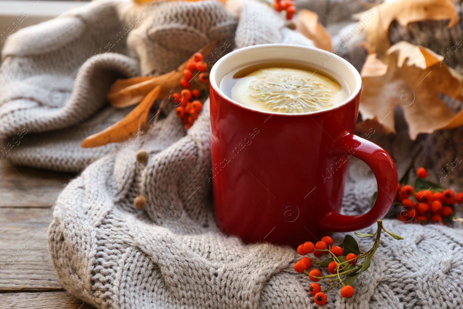 Photo of Cup of hot drink, sweater and autumn leaves on wooden table. Cozy atmosphere