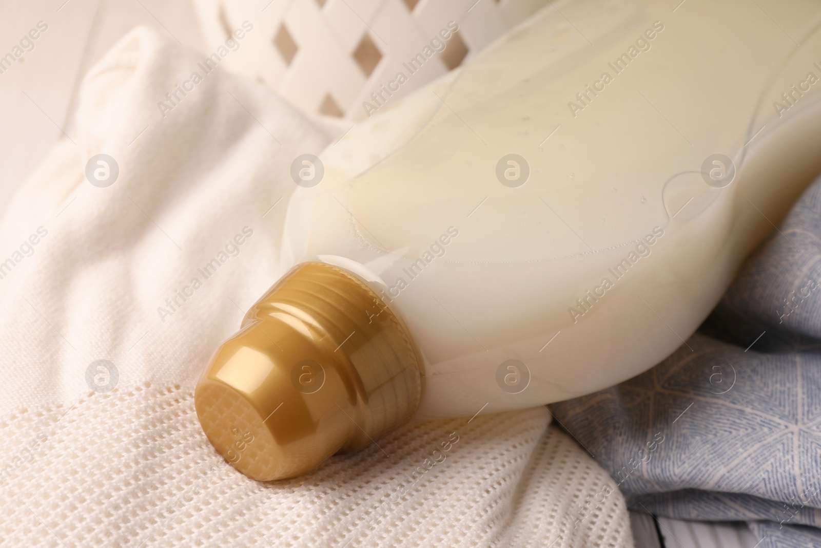 Photo of Bottle of fabric softener on clothes, closeup