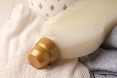 Photo of Bottle of fabric softener on clothes, closeup