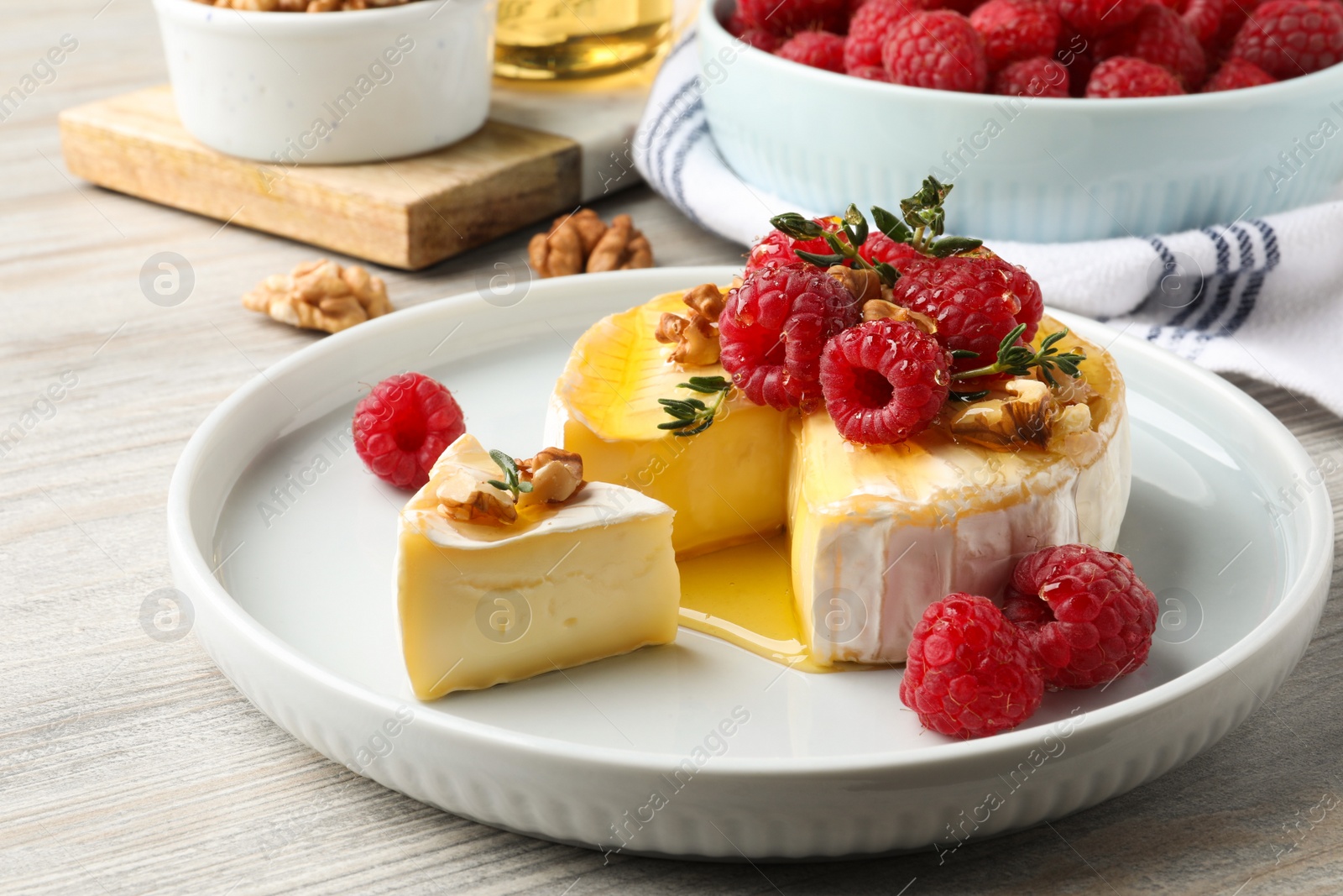 Photo of Brie cheese served with raspberries, walnuts and honey on white wooden table, closeup