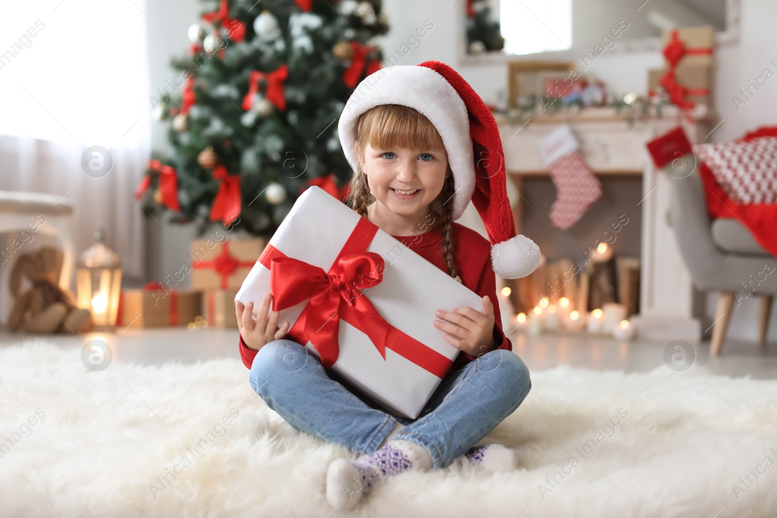 Photo of Cute little child in Santa hat with Christmas gift box at home