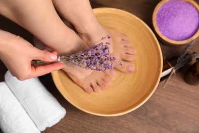 Photo of Woman holding lavender flowers and soaking her foot in bowl with water, top view. Pedicure procedure