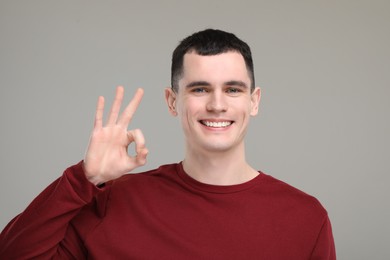 Photo of Handsome young man with clean teeth smiling and showing OK gesture on grey background