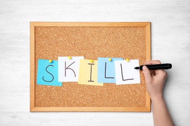 Photo of Woman writing word SKILL on sticky notes pinned to cork board. Business trainer concept