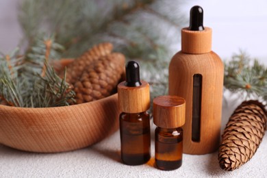Photo of Bottles of aromatic essential oil, pine branches and cones on light grey table, closeup