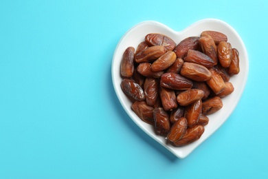 Photo of Heart shaped plate with sweet dried date fruits on color background, top view. Space for text