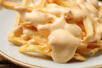 Photo of Delicious French fries with cheese sauce on table, closeup