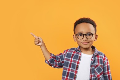 Photo of Cute African-American boy with glasses pointing on orange background. Space for text