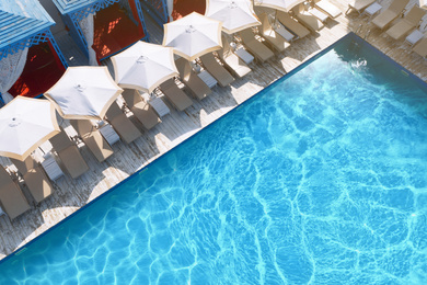 Image of Lounge chairs with umbrellas near swimming pool on sunny day 