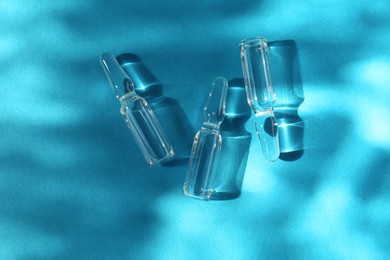 Photo of Skincare ampoules in sunlight on light blue background, top view