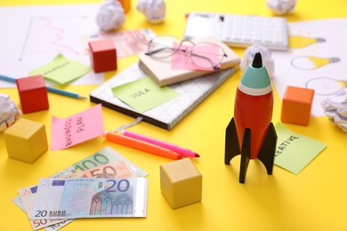Composition with toy rocket, stationery and money on yellow background. Startup concept