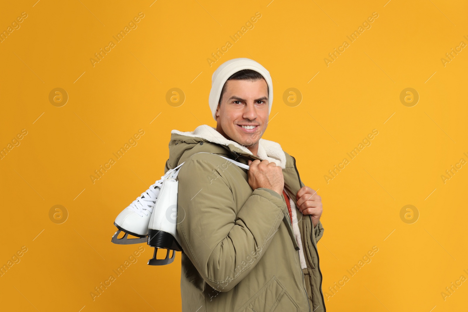 Photo of Happy man with ice skates on yellow background