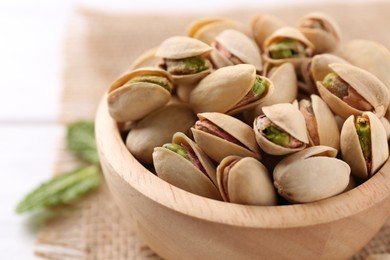 Photo of Tasty pistachios in bowl on white table, closeup