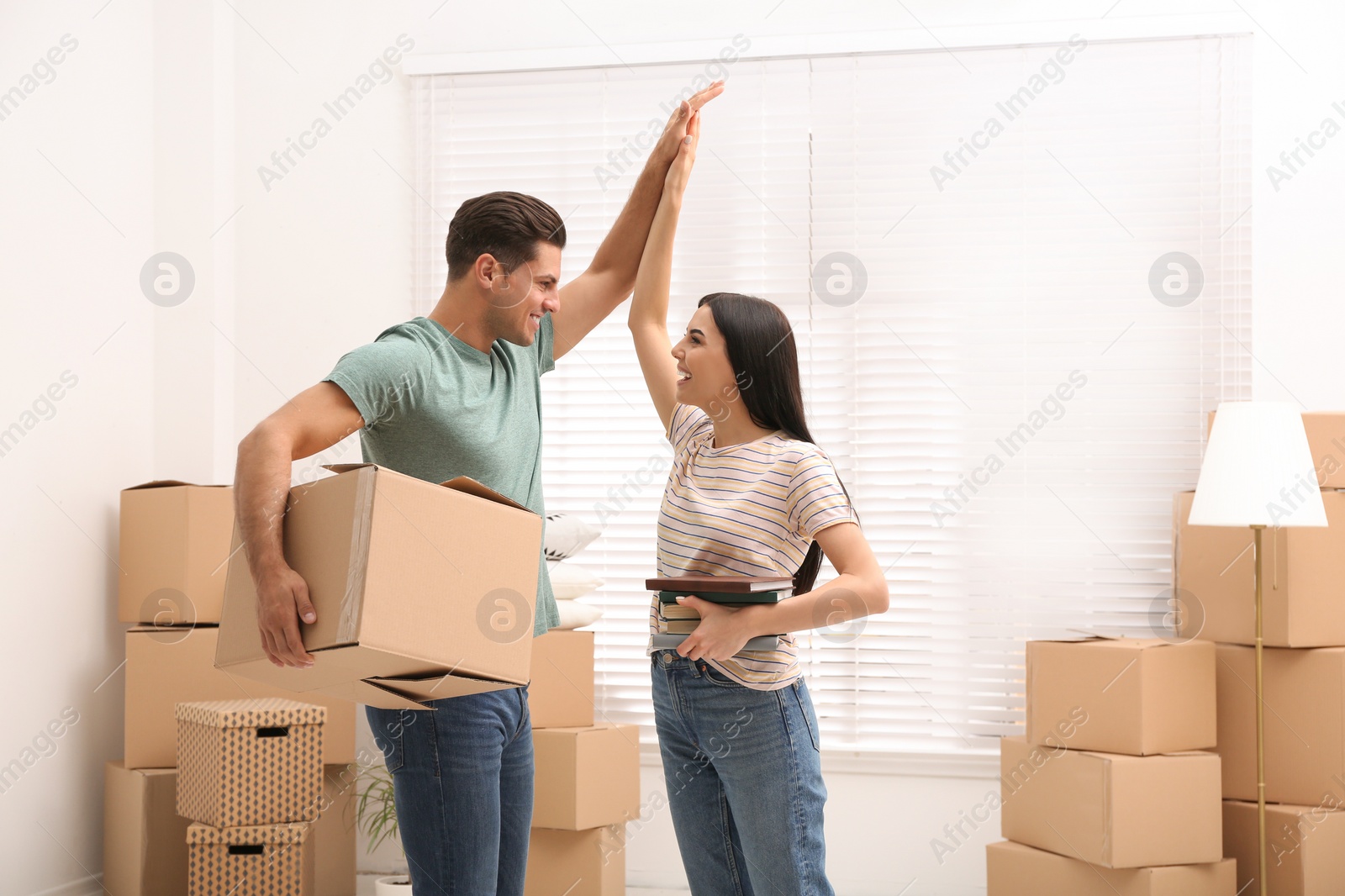 Photo of Happy couple in room with cardboard boxes on moving day