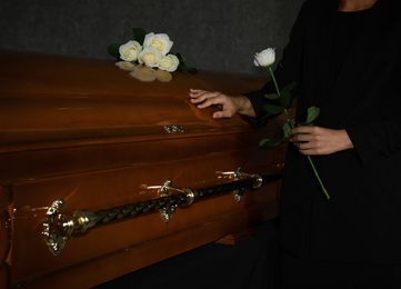 Photo of Young woman with white rose near casket in funeral home, closeup