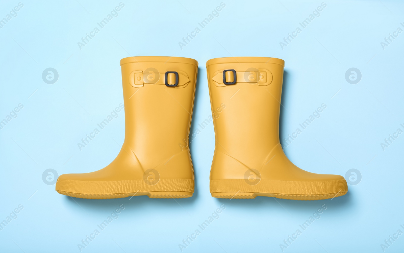 Photo of Pair of yellow rubber boots on light blue background, top view