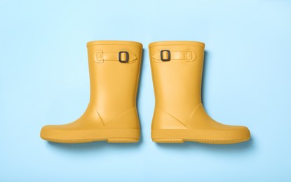 Photo of Pair of yellow rubber boots on light blue background, top view