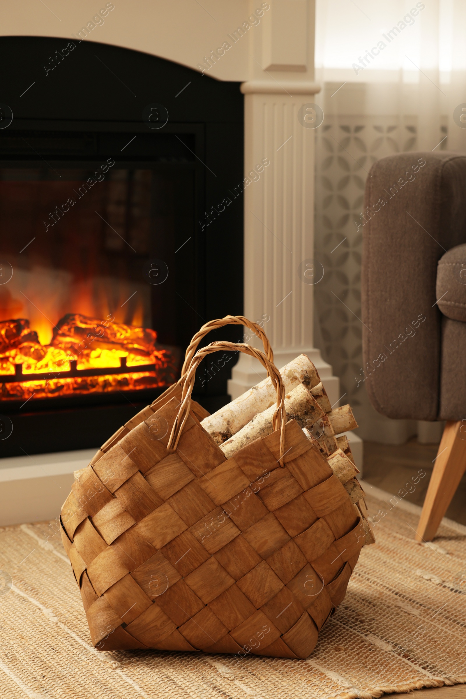 Photo of Wicker basket with wood near fireplace in room