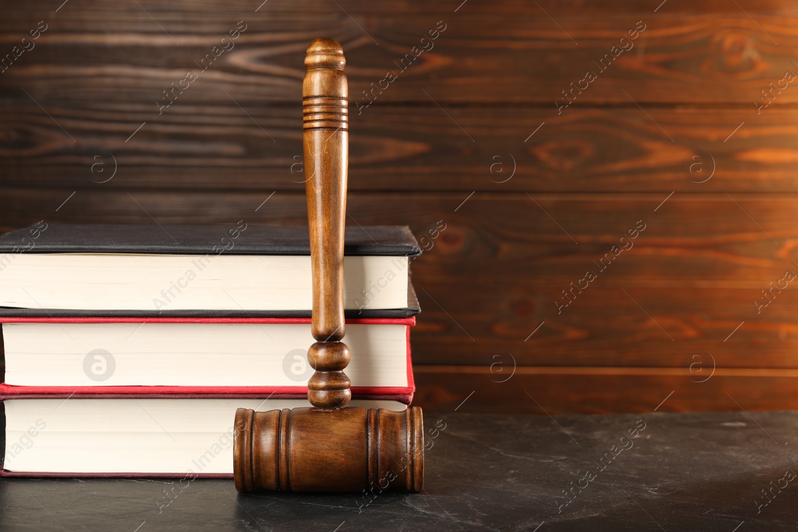 Photo of Wooden gavel and stack of books on dark textured table, closeup. Space for text