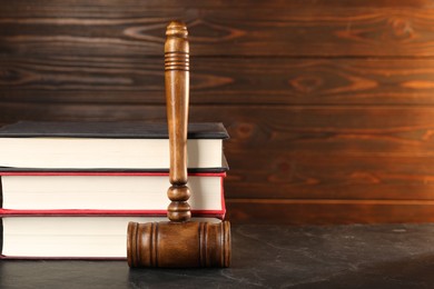 Photo of Wooden gavel and stack of books on dark textured table, closeup. Space for text