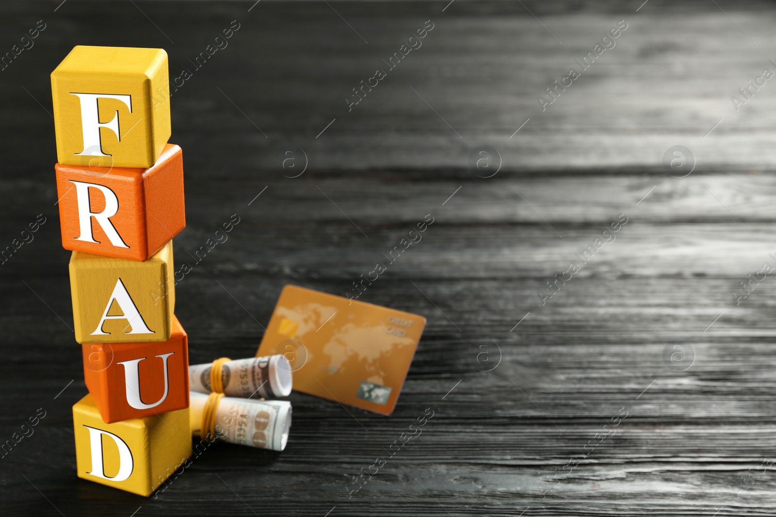 Photo of Cubes with word Fraud, credit card and rolled dollar banknotes on black wooden background. Space for text