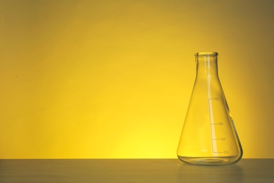 Photo of Conical flask with liquid on table against color background. Chemistry laboratory glassware