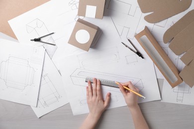 Photo of Woman creating packaging design at light wooden table, top view