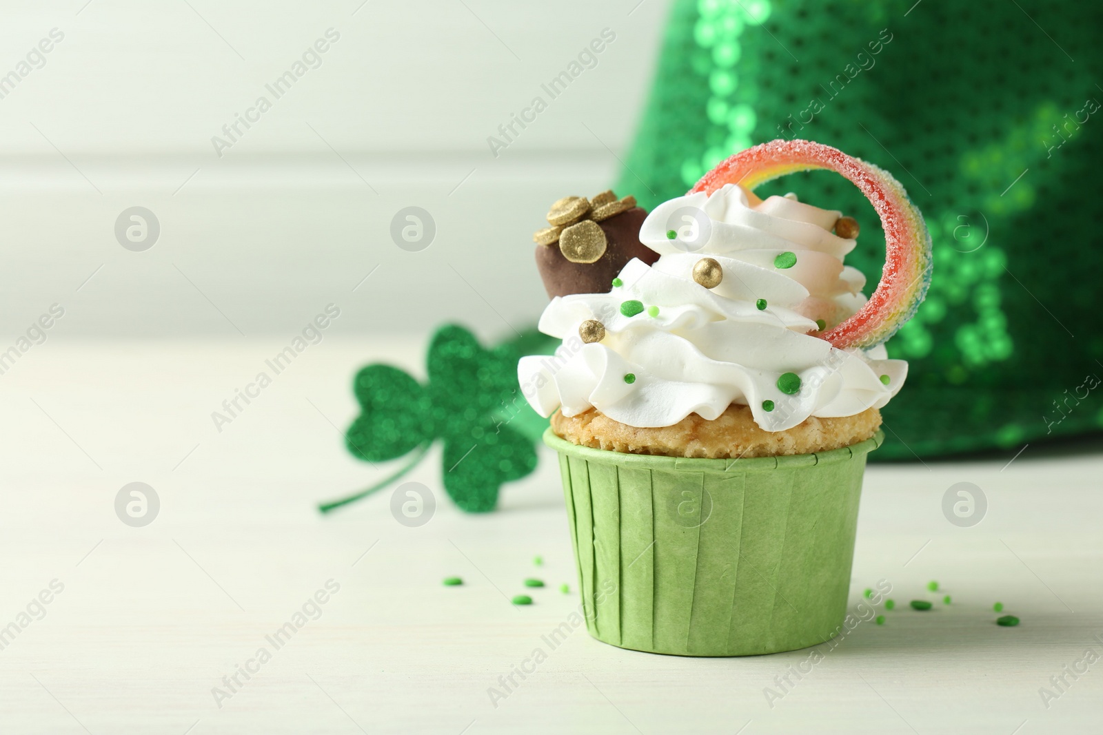 Photo of St. Patrick's day party. Tasty cupcake with sour rainbow belt and pot of gold toppers on white table, closeup. Space for text