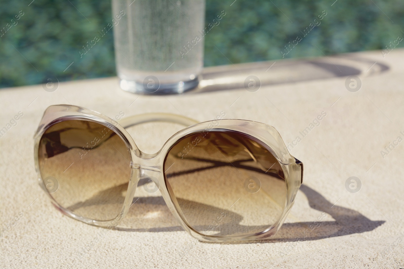 Photo of Stylish sunglasses near outdoor swimming pool on sunny day, closeup