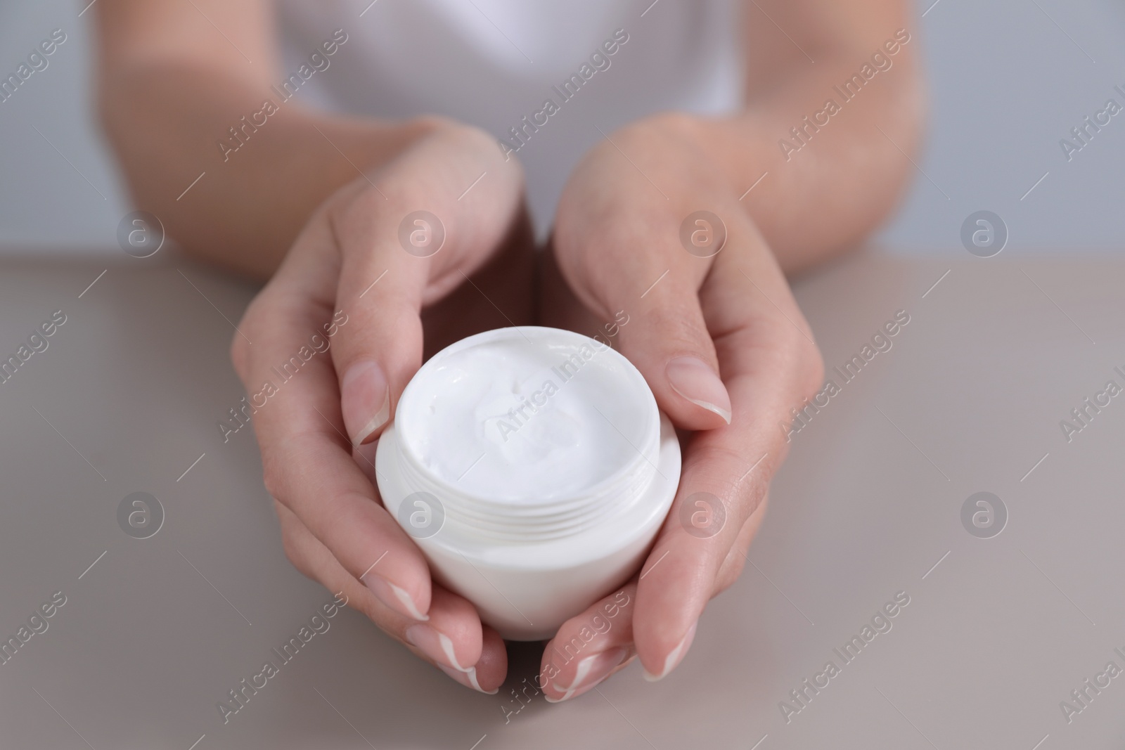 Photo of Young woman holding jar of cream at table, closeup