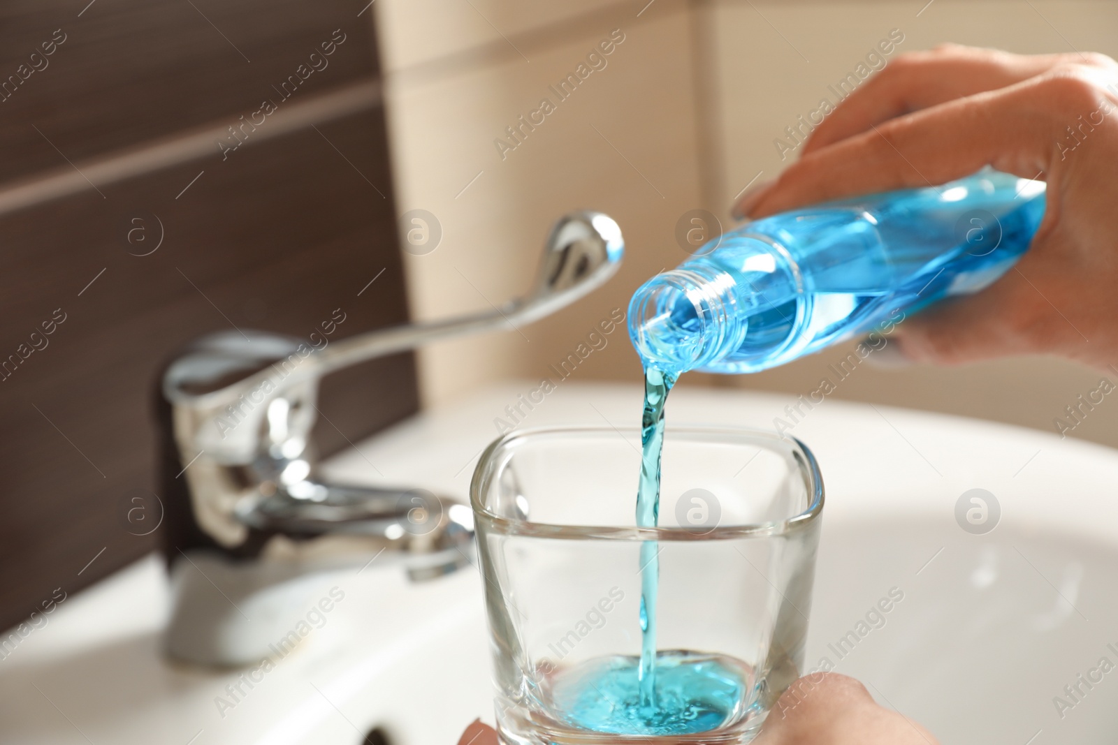 Photo of Woman pouring mouthwash from bottle into glass in bathroom, closeup. Teeth care