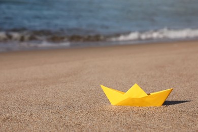 Yellow paper boat near sea on sandy beach, space for text