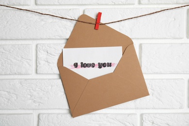 Photo of Envelope with I Love You card hanging on twine near white brick wall