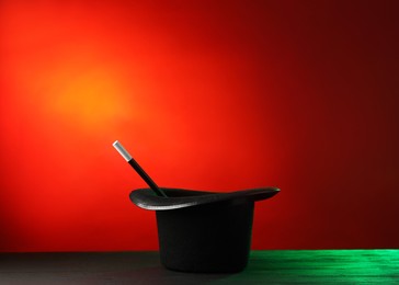 Photo of Magician's hat and wand on black wooden table against color background, space for text