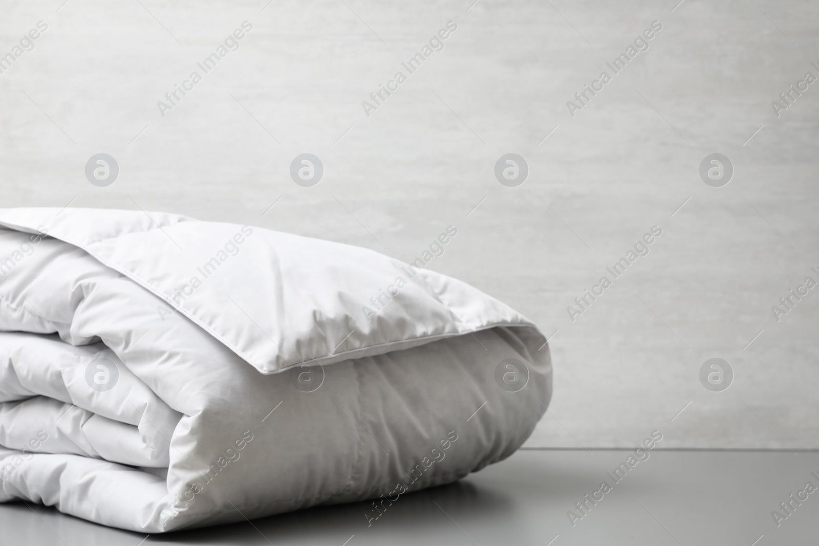 Photo of Soft folded blanket on light grey table, closeup. Space for text