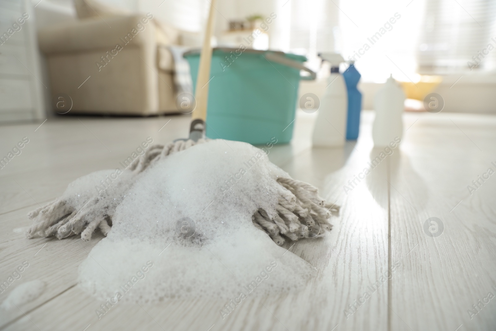 Photo of Mop with foam indoors. Bucket and different cleaning products on background