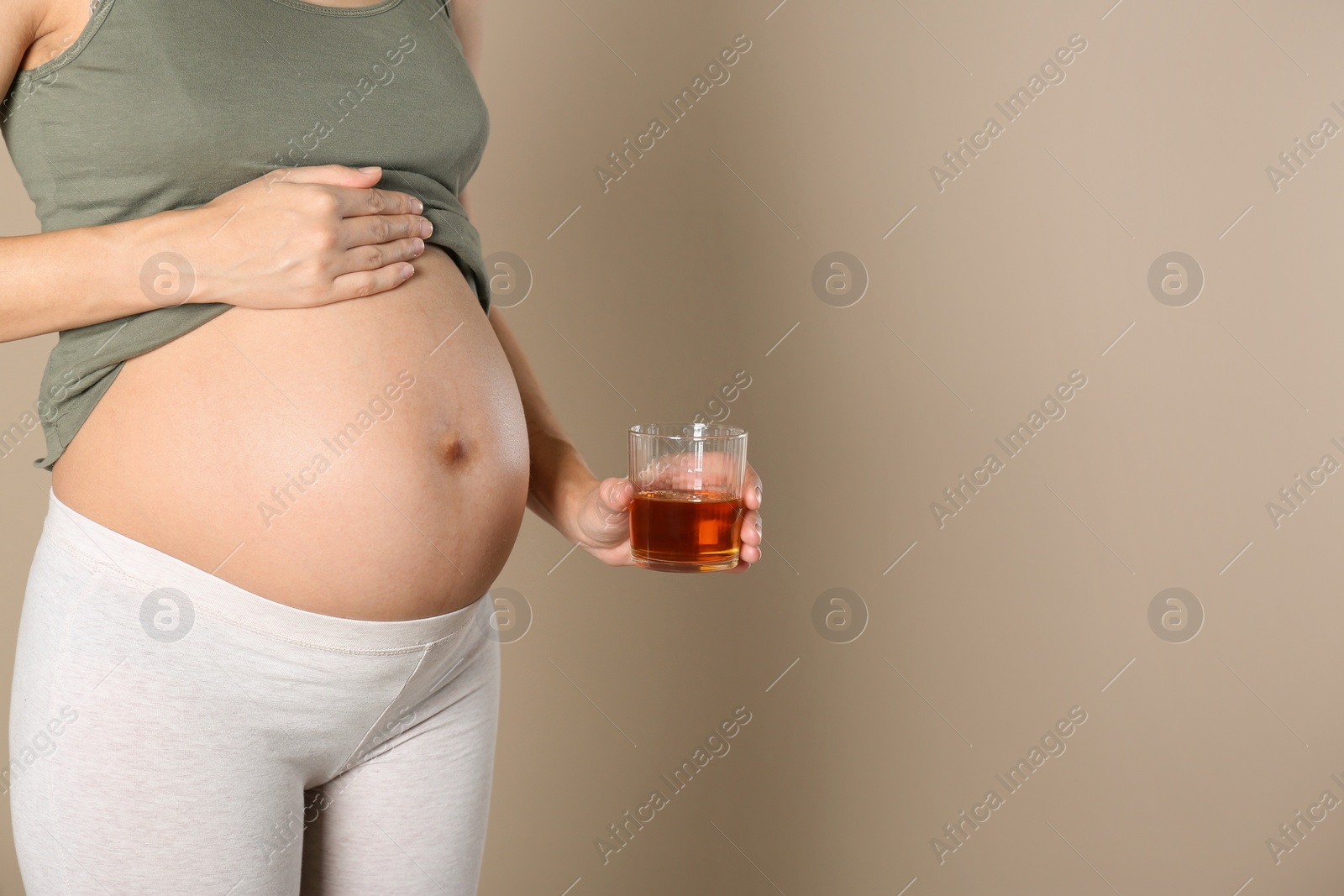 Photo of Pregnant woman with glass of whiskey on color background, space for text. Alcohol addiction