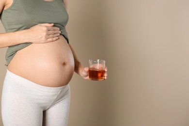 Photo of Pregnant woman with glass of whiskey on color background, space for text. Alcohol addiction