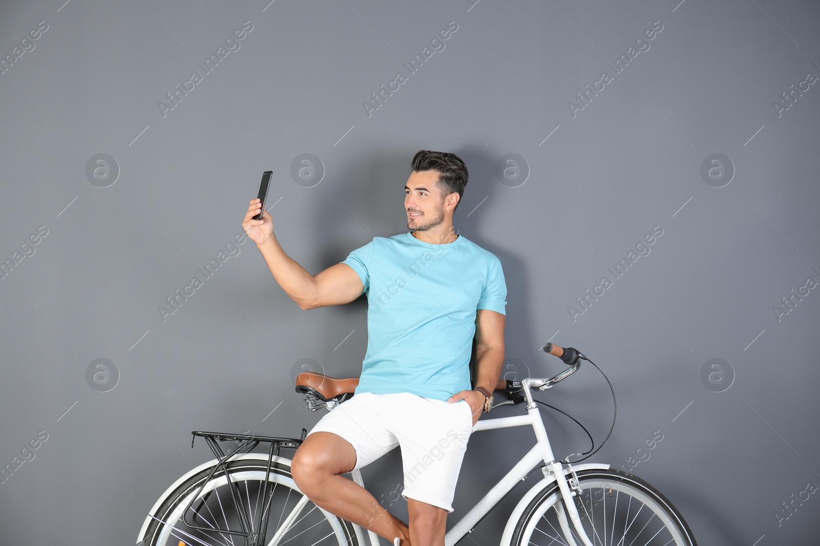 Photo of Handsome young hipster man taking selfie with bicycle on color background