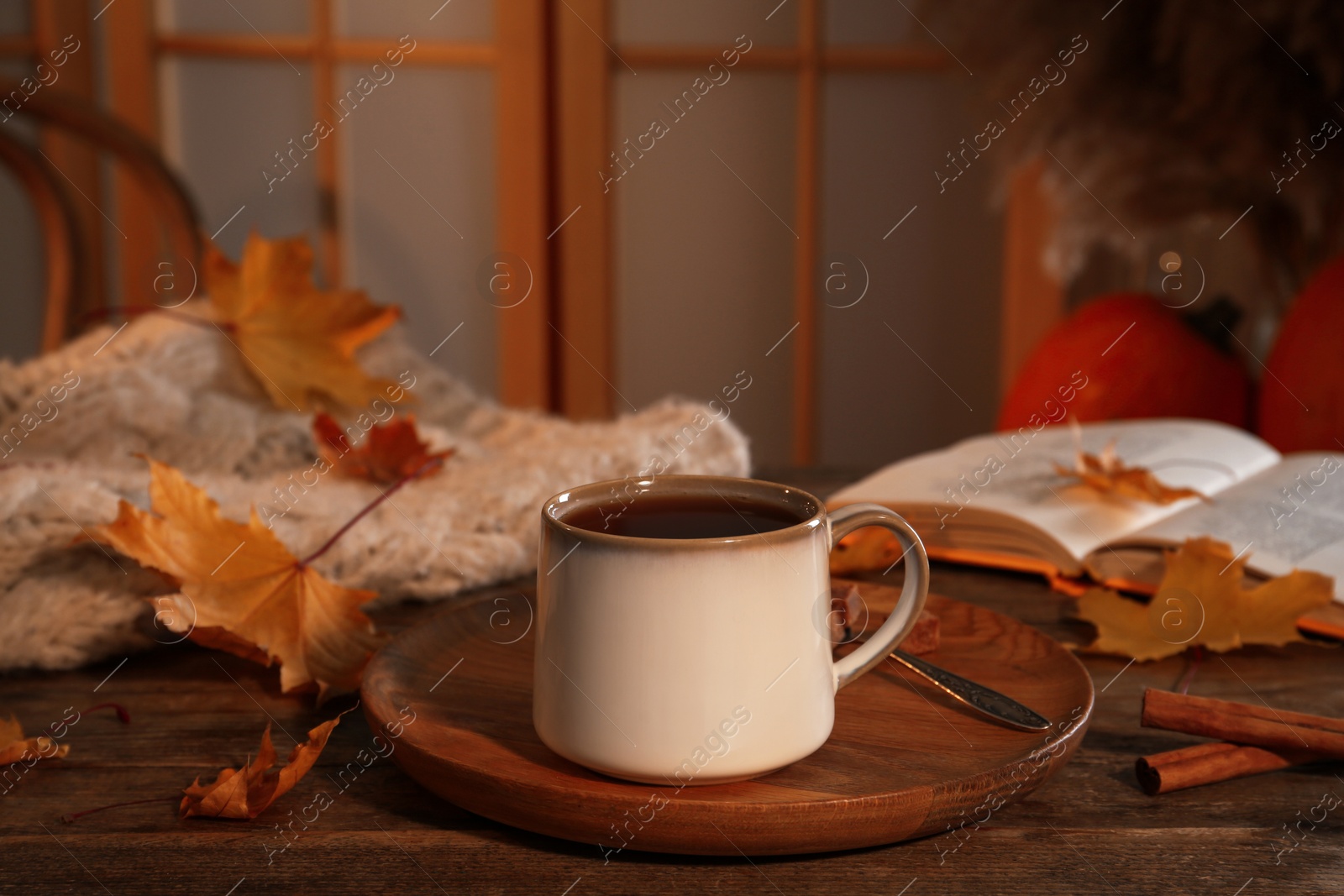 Photo of Cup of aromatic tea, sweater, book and autumn leaves on wooden table indoors, space for text