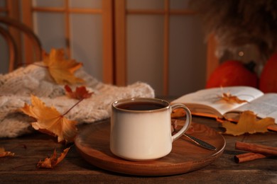 Cup of aromatic tea, sweater, book and autumn leaves on wooden table indoors, space for text