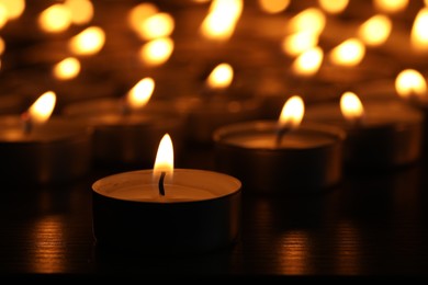 Photo of Burning candles on wooden table in darkness, closeup