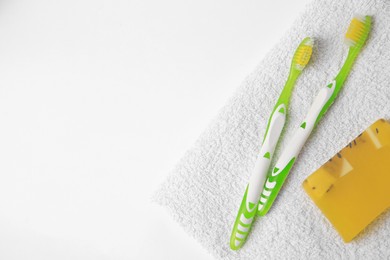 Photo of Light green toothbrushes, terry towel and solid soap on white background, top view. Space for text