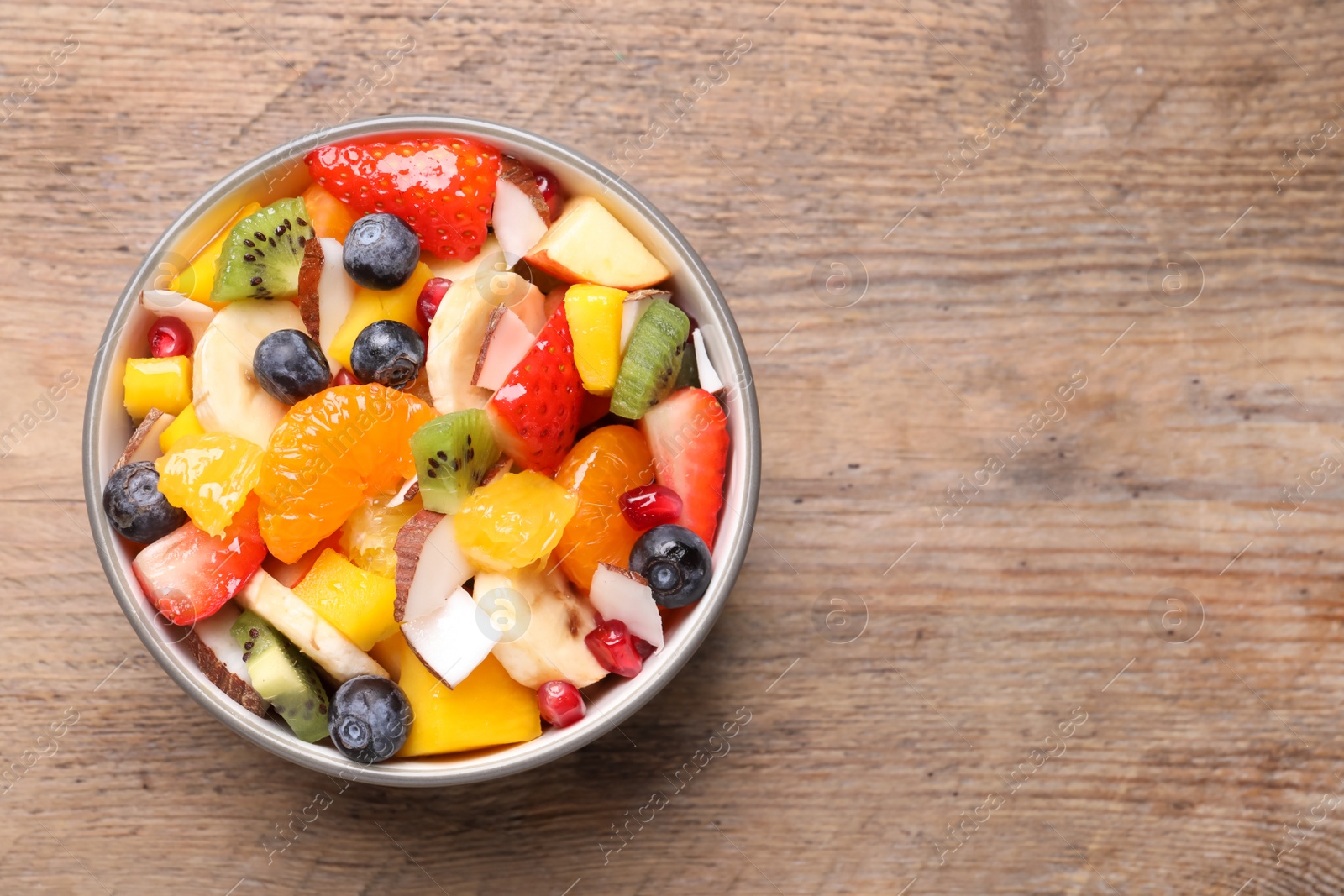 Photo of Delicious fresh fruit salad in bowl on wooden table, top view. Space for text