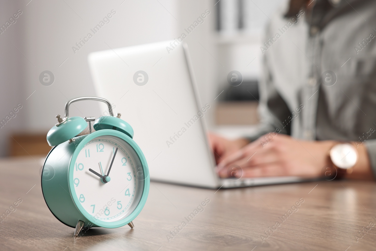 Photo of Turquoise alarm clock and man working at table in office, closeup with space for text. Deadline concept